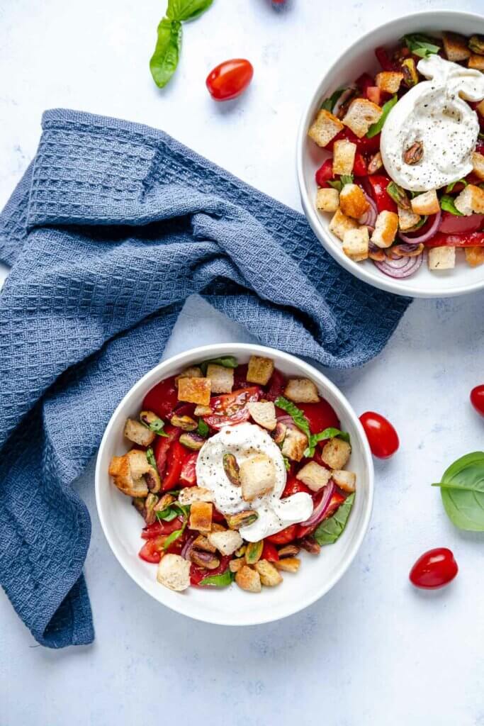 Tomaten-Burrata-Salat mit Pistazien-Croutons in zwei Portionen aufgeteilt.